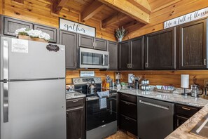 A modern kitchen with dark wood cabinets, stainless steel appliances, and a marble countertop. - Sleeps 6, Hot Tub, Arcade Loft, Kids Play Tent, 3.6 Mi to Dollywood (Sevierville)