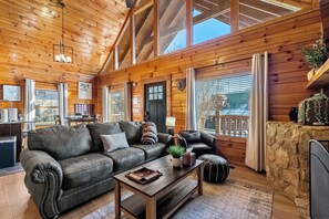 A cozy cabin interior with a leather sofa, a wooden coffee table, and a stone fireplace. - Hot Tub & Play Tent | Near Dollywood (Sevierville)