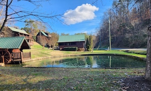 A rustic cabin with a green roof, a pond, and a forested area. - Sleeps 6, Hot Tub, Arcade Loft, Kids Play Tent, 3.6 Mi to Dollywood (Sevierville)