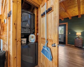 A wooden interior with a kitchen area, including a refrigerator, a sink, and a broom leaning against a door. - Sleeps 6, Hot Tub, Arcade Loft, Kids Play Tent, 3.6 Mi to Dollywood (Sevierville)