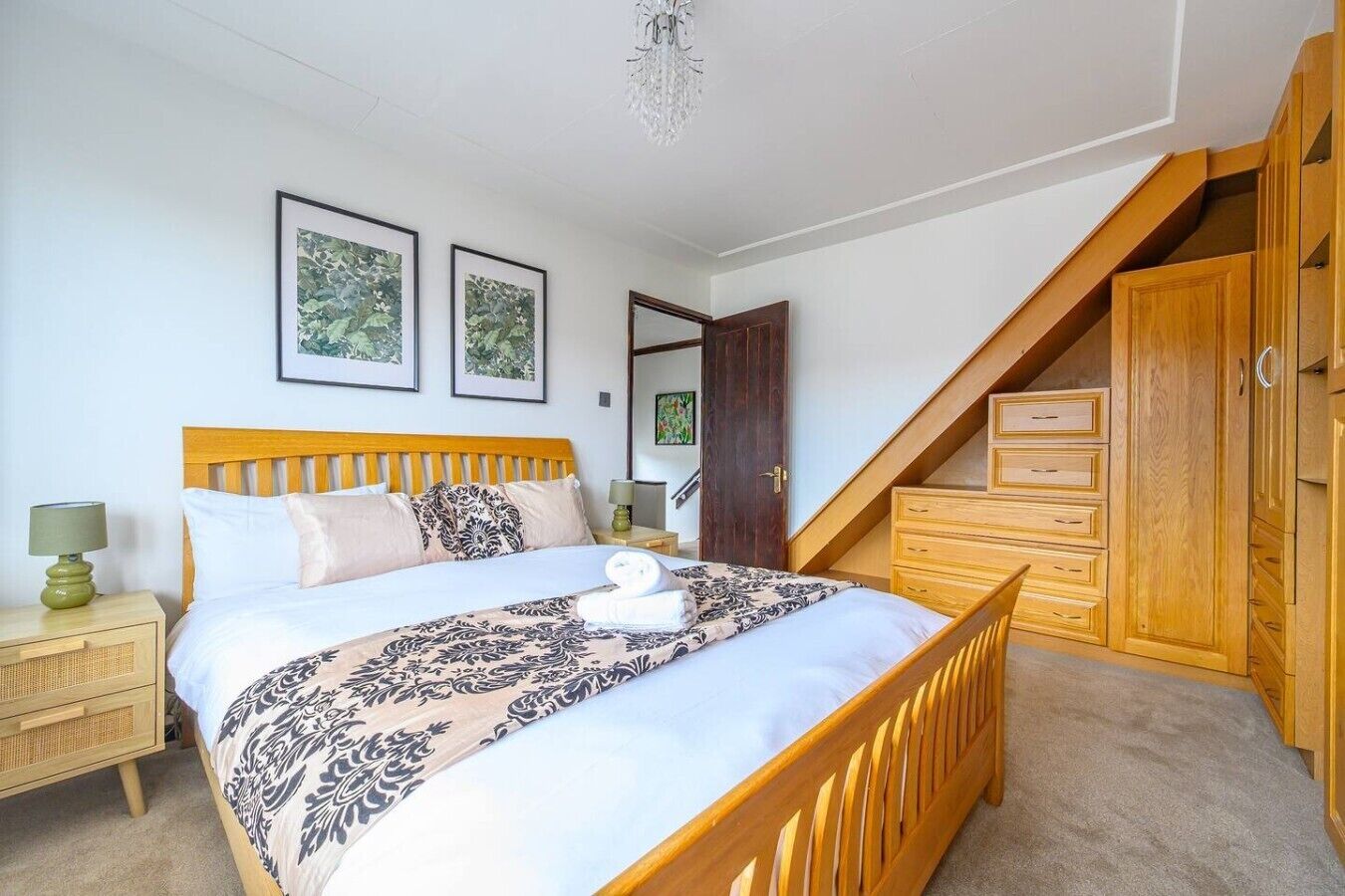 A bedroom with a bed, wooden headboard, a nightstand, a dresser, a wardrobe, and a staircase.
