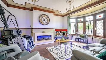 A living room with a fireplace, a television, and a large clock on the wall.