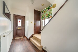 Een hal met een houten deur, een witte radiator en een wenteltrap met tapijt.