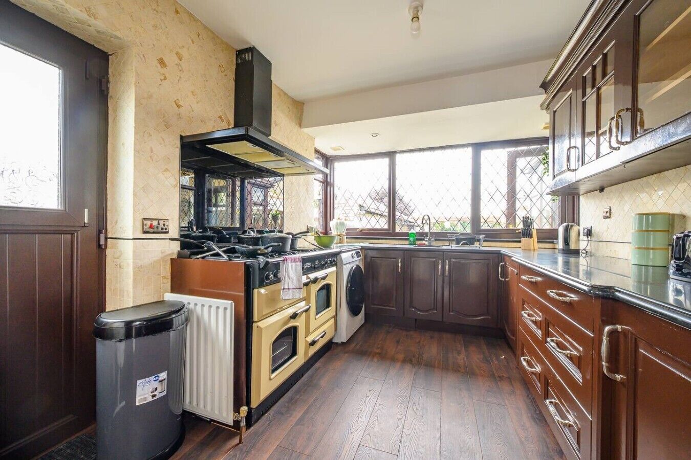 Een keuken met een kookplaat, oven en wasmachine, houten keukenkastjes en een raam.