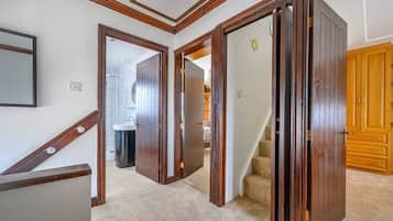 A hallway with wooden doors, a staircase, and a bathroom visible in the background.