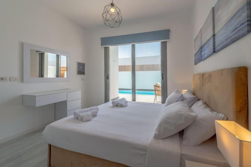 A hotel room with a bed, a bedside table, a mirror, a window with a view of the pool, and a ceiling light fixture.