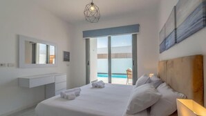 A hotel room with a bed, a bedside table, a mirror, a window with a view of the pool, and a ceiling light fixture. - Luxury Villa with private pool Sholan 2 (Red Sea Governorate)