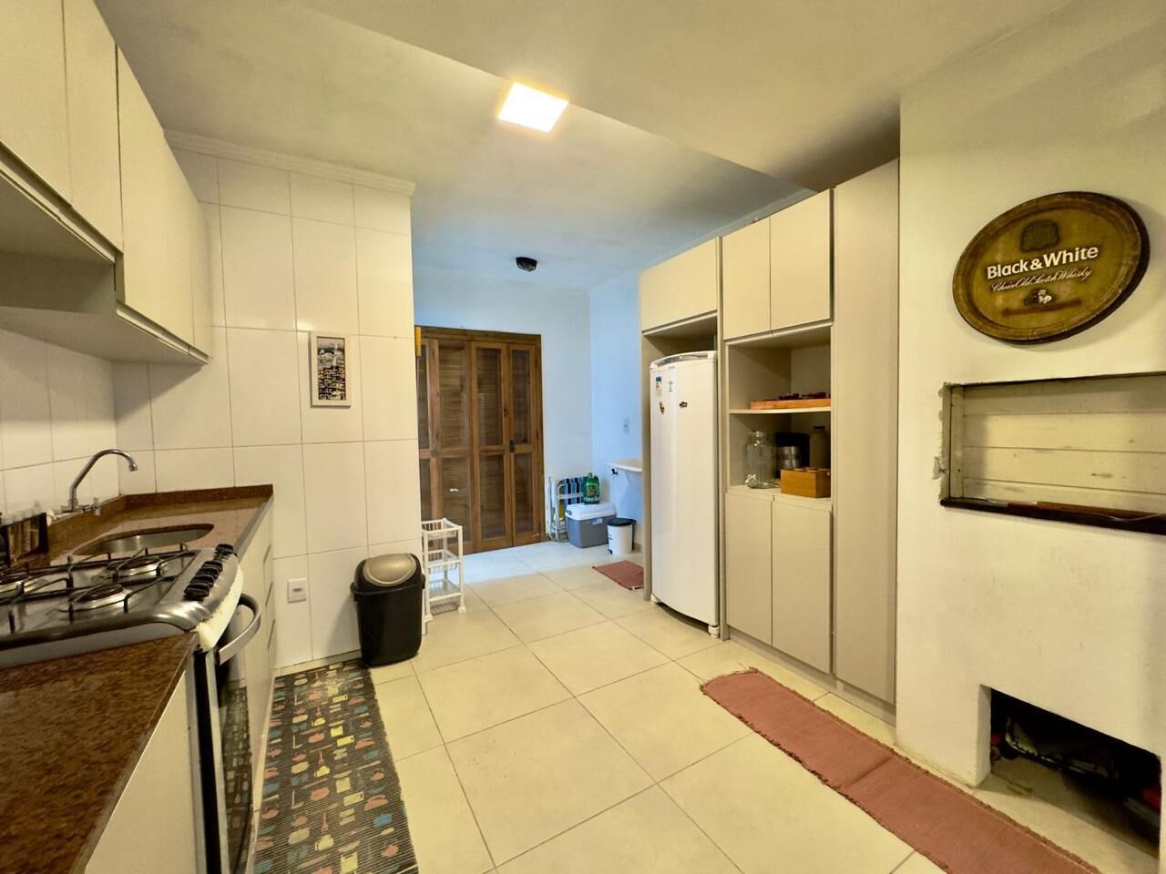 Uma cozinha com fogão a gás, armários brancos, uma geladeira e uma placa na parede.