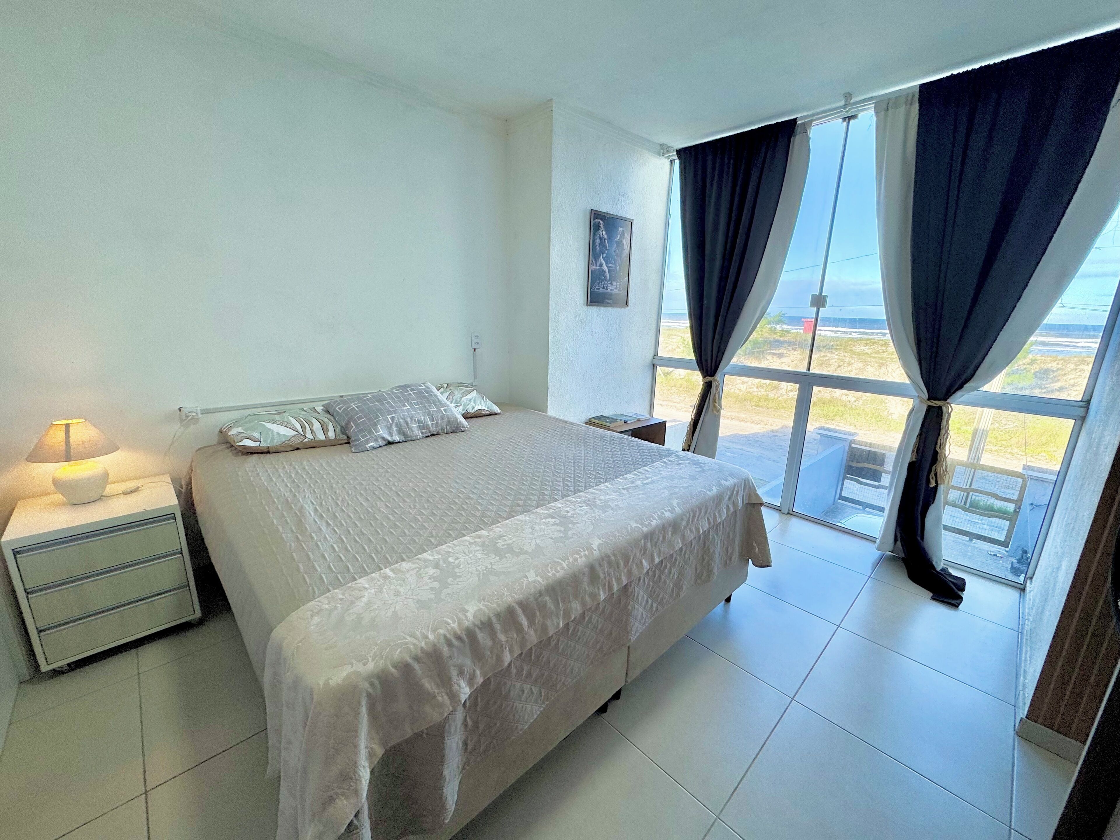 A bedroom with a bed, nightstand, lamp, and a view through large windows.