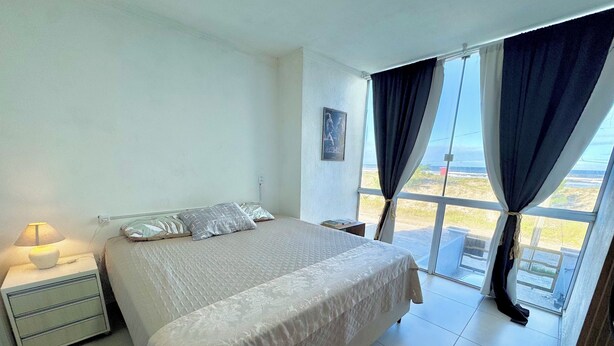 Un dormitorio con cama, mesita de noche, lámpara y vistas amplias a través de grandes ventanales.