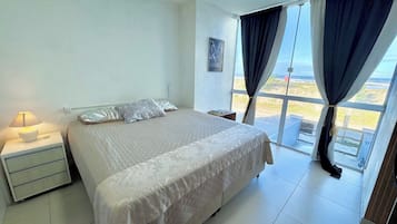 A bedroom with a bed, nightstand, lamp, and a view through large windows.