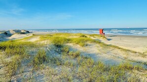 Una playa con dunas, una torre roja de salvavidas y el océano al fondo.