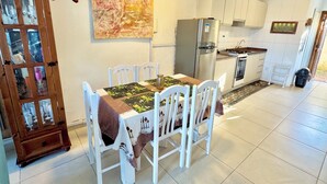 A kitchen with white cabinets, a refrigerator, a stove, and a dining table with chairs. - Cinematic view, 2 suites, beachfront. (Imbé)