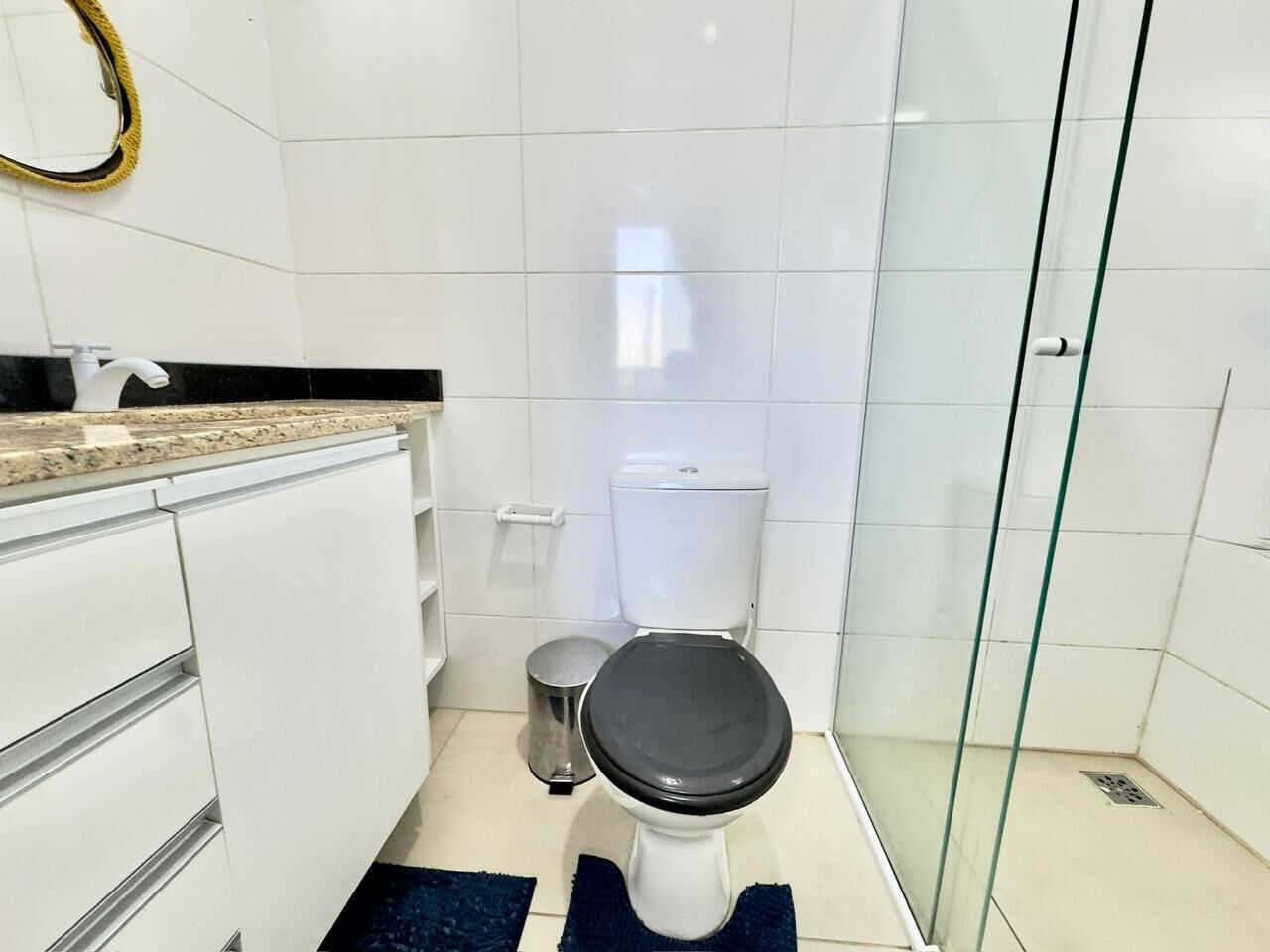 Casa de banho moderna com sanita, um contentor de lixo, cabine de duche em vidro e bancada com lavatório.