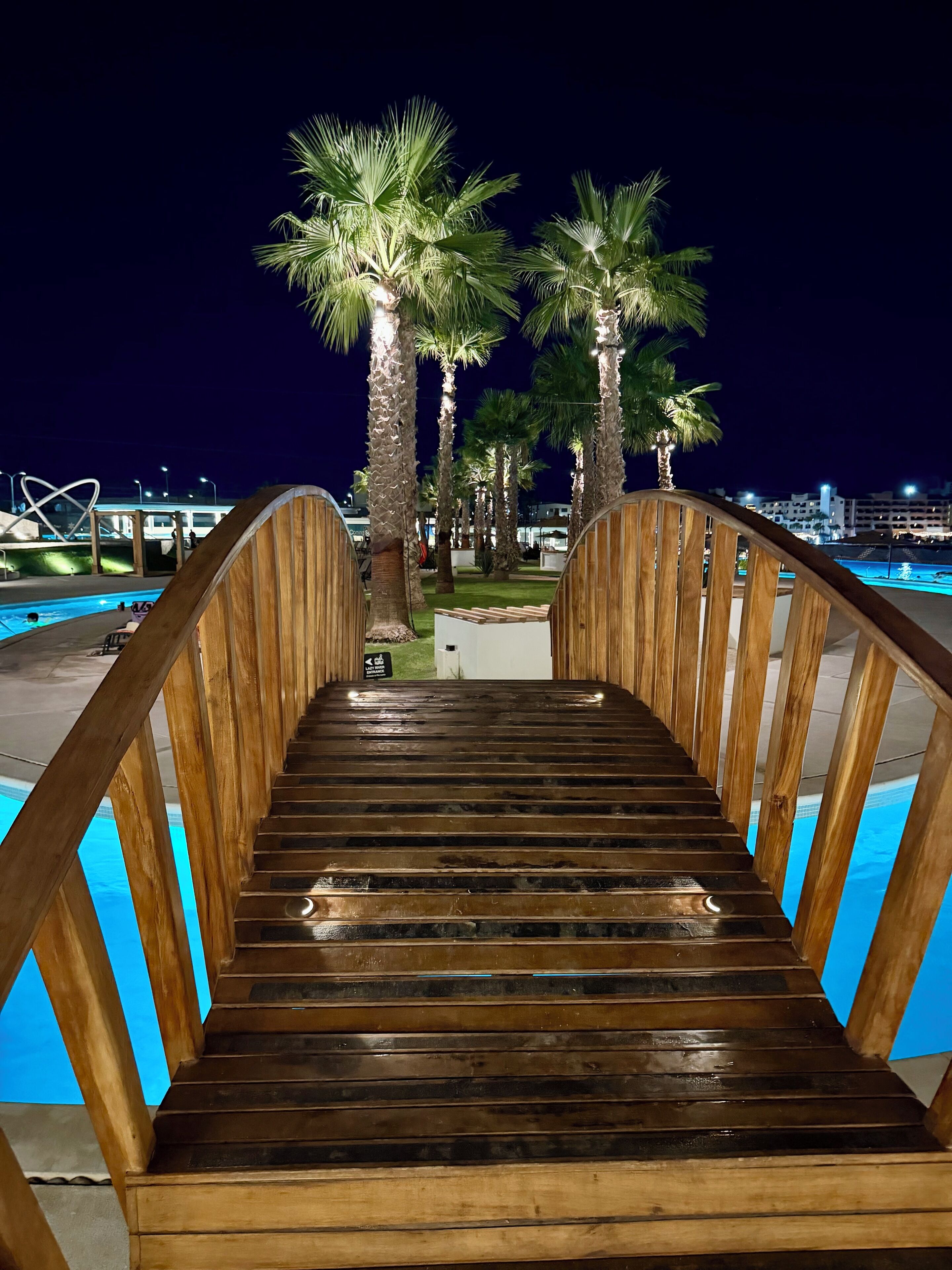 Una scala di legno conduce a una zona piscina, sullo sfondo si vedono palme.