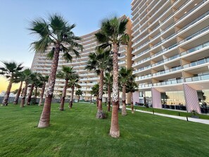 A modern hotel with multiple floors, palm trees, and a well-maintained lawn. - Luxury Couples Retreat - Sonoran Star Beachfront (Puerto Peñasco)