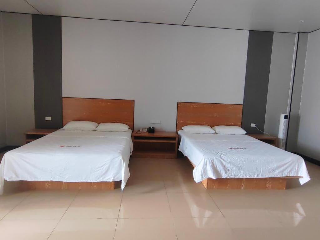 A hotel room with two single beds, a wooden headboard, a bedside table, and a wall-mounted air conditioning unit.