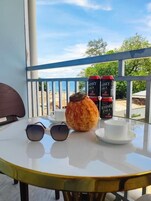Mesa redonda com uma chávena branca, um copo de bebida e uma lata de bebida numa varanda com guarda.
