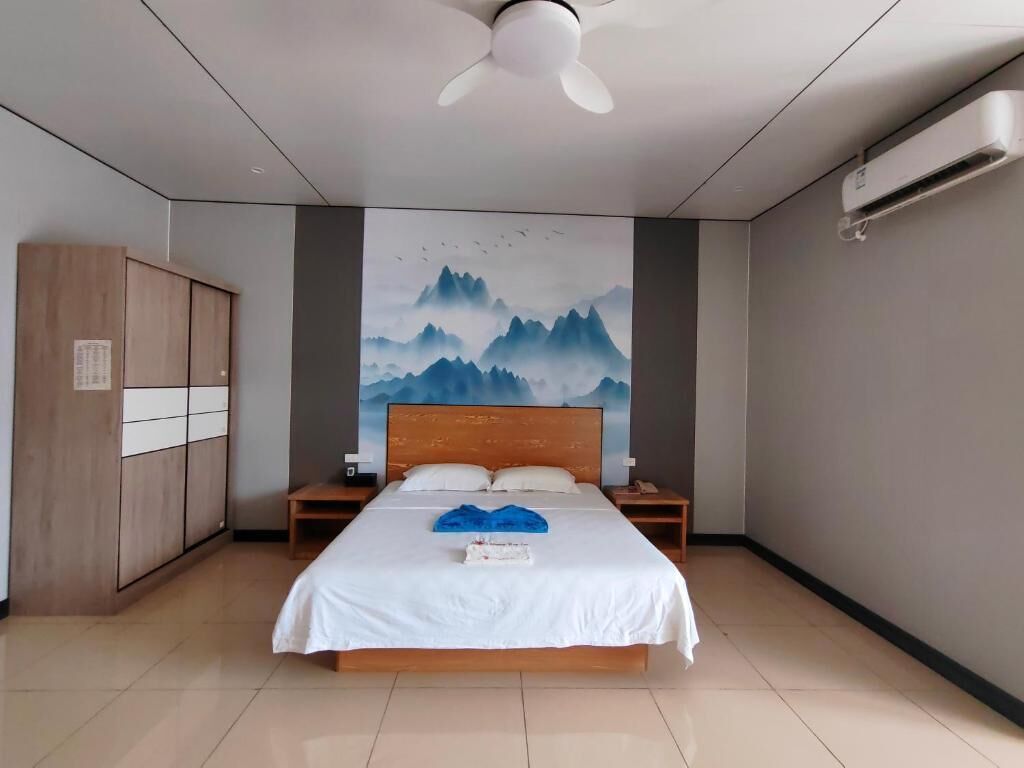 Habitación de hotel con cama, ventilador de techo, aire acondicionado instalado en la pared y armario de madera.
