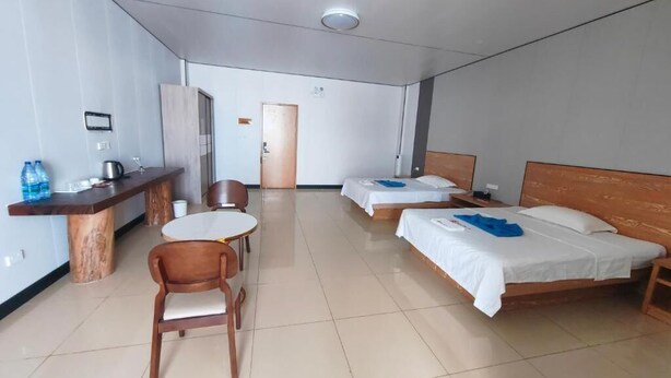 Ein Hotelzimmer mit zwei Betten, einem kleinen runden Tisch, einem Holzstuhl, einem Schreibtisch mit Wasserkocher und Wasserspender.