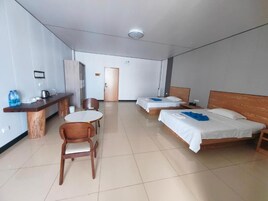 Quarto de hotel com duas camas, uma mesa redonda pequena, uma cadeira de madeira, uma escrivaninha com chaleira e um dispensador de água.