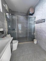 Uma casa de banho moderna com cabine de duche em vidro, uma sanita e uma pia branca.