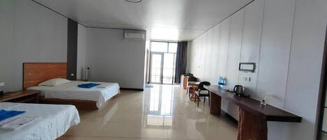 A hotel room with two beds, a desk, a chair, a small table, a window, and a bathroom.