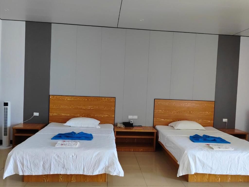Een hotelkamer met twee bedden, houten hoofdborden, witte beddengoed en een klein nachtkastje met een lamp.