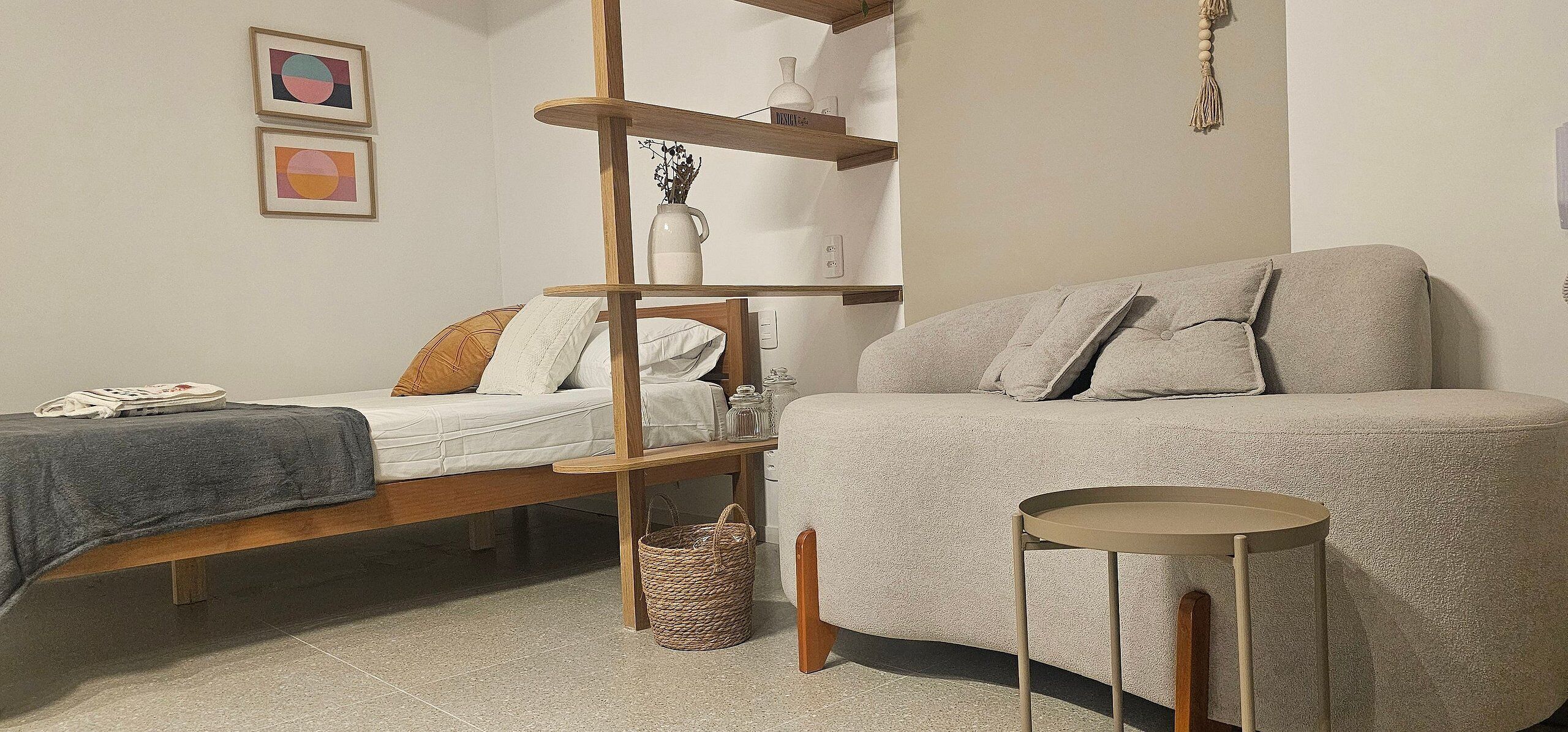 A bedroom with a bed, a sofa, a wooden shelf unit, and a small round table.