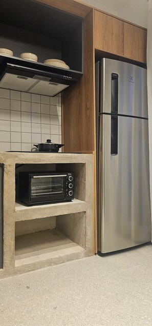 A kitchen with a built-in oven, a stainless steel refrigerator, and a tiled backsplash. - Cond. Metro Casa Centro 101 (São Paulo)