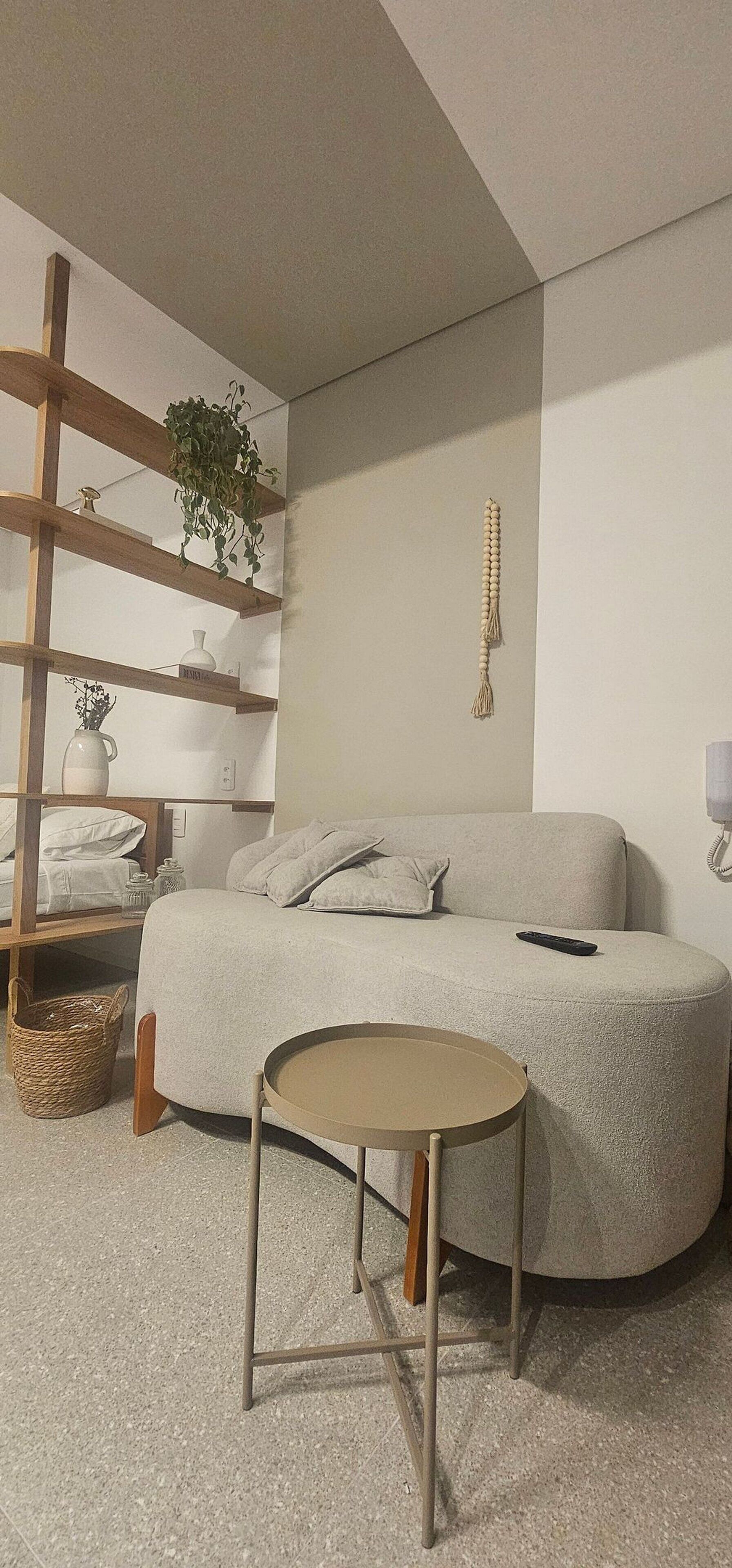 Un dormitorio acogedor con una cama curvada, una mesita redonda pequeña, un estante de madera con plantas y un teléfono montado en la pared.