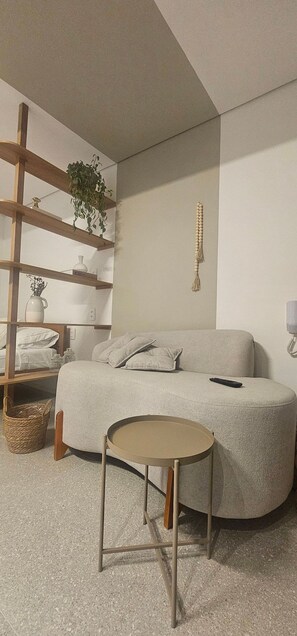 A cozy bedroom with a curved bed, a small round table, a wooden shelf with plants, and a wall-mounted telephone. - Cond. Metro Casa Centro 101 (São Paulo)