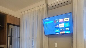 Habitació amb televisió de pantalla plana penjada a la paret, una taula petita amb cadires, un frigorífic i un aire condicionat.