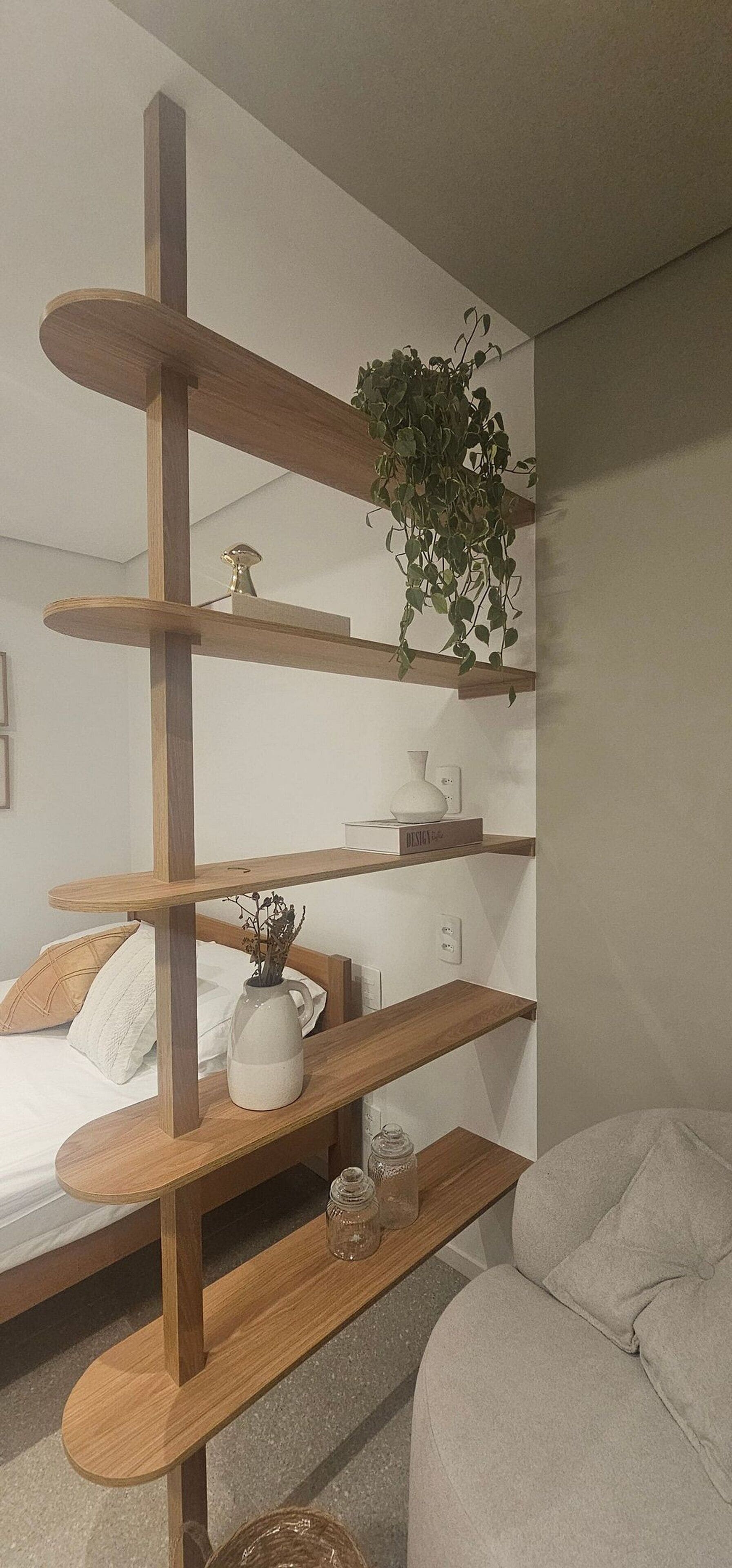 A room with a bed, a wooden shelf unit, a potted plant, and a white vase.