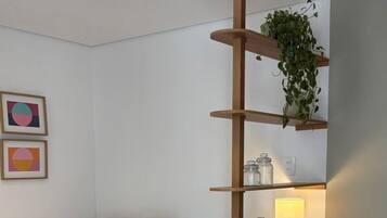 Een moderne slaapkamer met een bed, een nachtkastje met een lamp, een houten plank met een plant en een klein mandje.