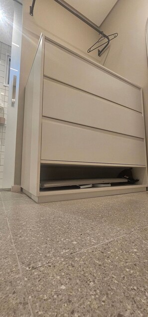 A beige cabinet with a shelf, a metal hook on the wall, and a tiled floor. - Cond. Metro Casa Centro 101 (São Paulo)