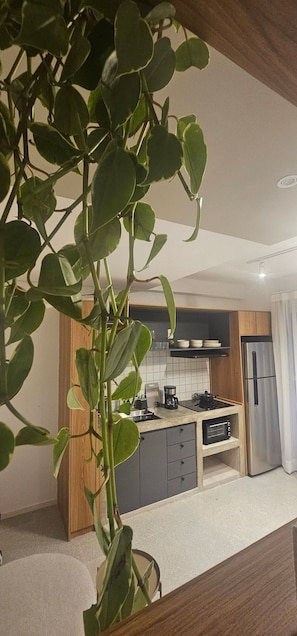 A modern kitchen with a central island, wooden cabinets, and a stainless steel refrigerator. - Cond. Metro Casa Centro 101 (São Paulo)