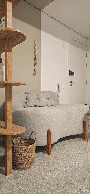 A neutral-toned room with a bed, a wooden shelf, a woven basket, and a door with a lock. - Cond. Metro Casa Centro 101 (São Paulo)