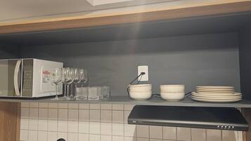 Una cocina con microondas, copas de vino, cuencos y cafetera.