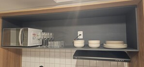 A kitchen with a microwave, wine glasses, bowls, and a coffee maker. - Cond. Metro Casa Centro 101 (São Paulo)
