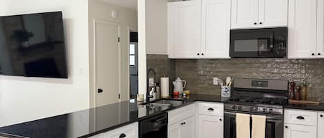 A modern kitchen with white cabinets, a black countertop, and a stainless steel stove.