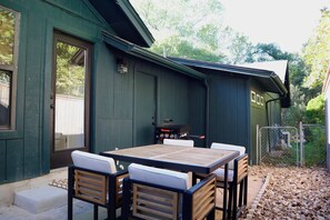 An outdoor patio with a table and chairs, a barbecue grill, and a green building with a door. - Stay Smooth ATX/ Stylish,Quiet Home Base Near the Domain. (Austin)
