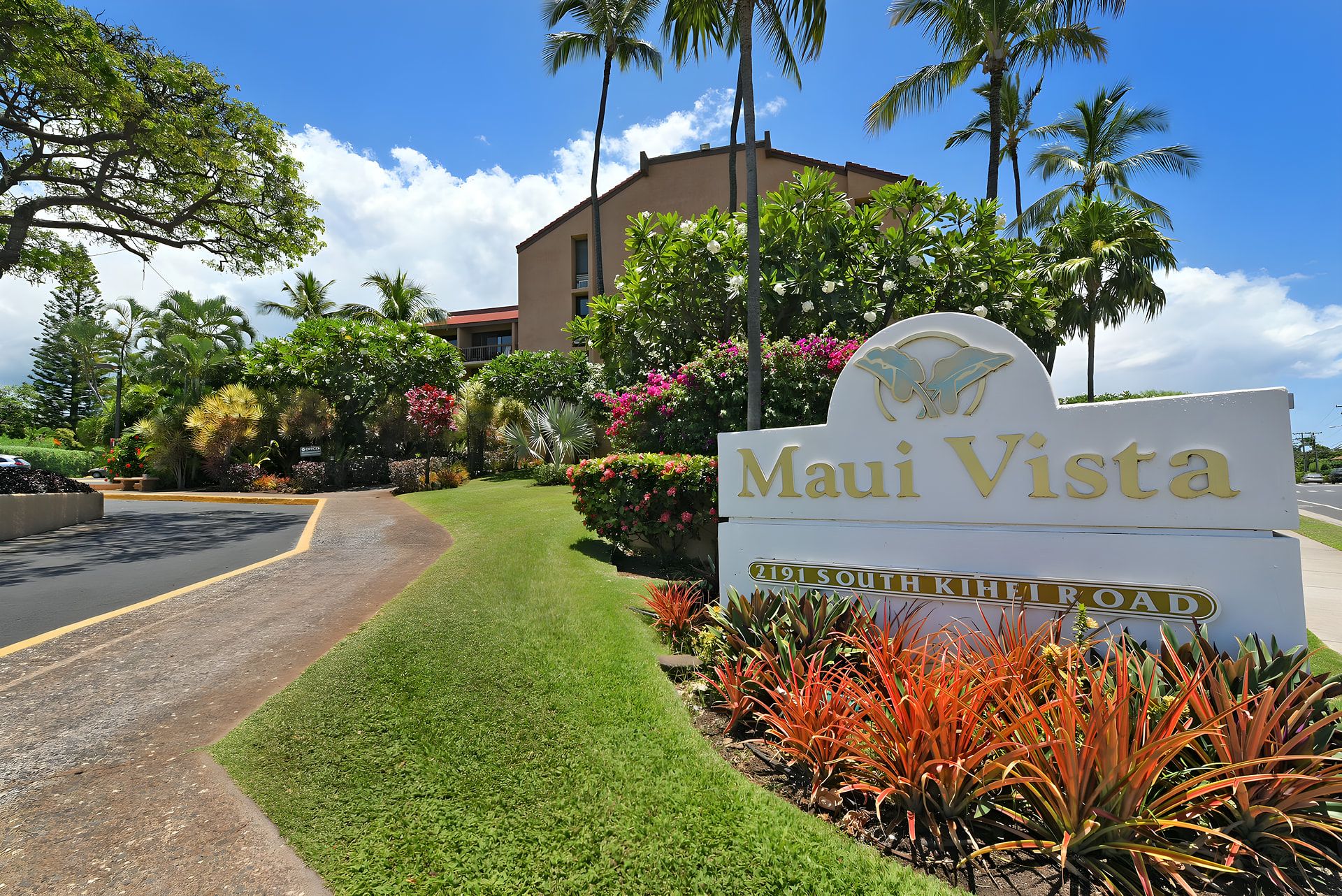 A sign for 'Maui Vista' with a clear road leading to a building, surrounded by lush greenery and palm trees.