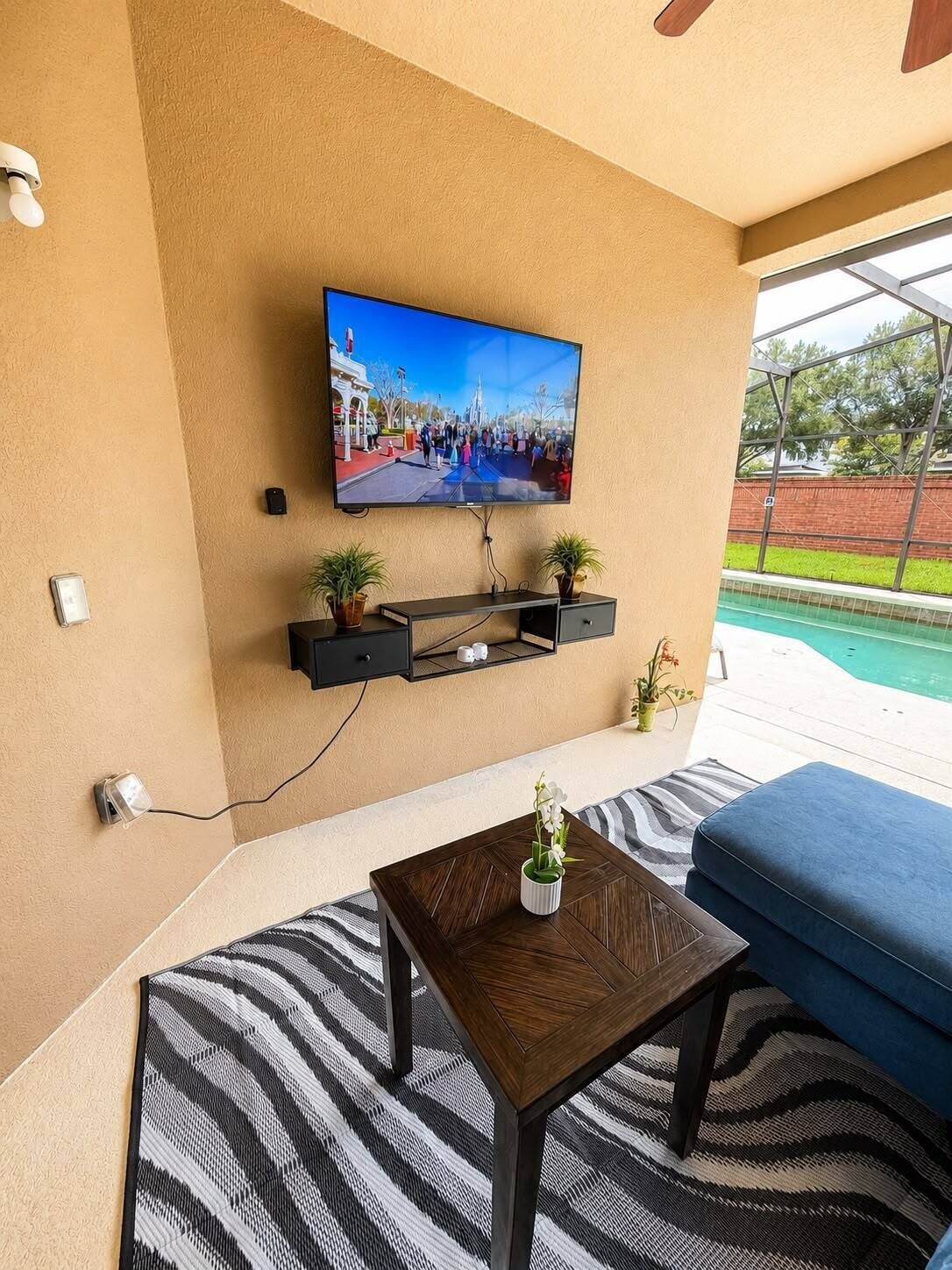 Ein modernes Wohnzimmer mit einem an der Wand befestigten Flachbildfernseher, einem kleinen Tisch mit einer Vase und einem blauen Sofa.
