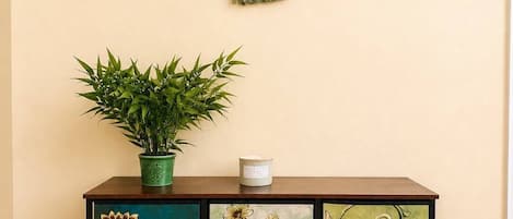 A wooden cabinet with floral and abstract designs, a green macrame hanging, and a potted plant on top.