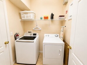 A laundry room with a front-loading washer and dryer, a shelf with laundry supplies, and a fire extinguisher. - Family Villa, Private pool, cinema, and game room. (Davenport)