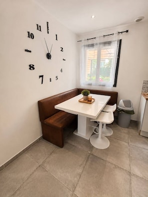 A modern kitchen with a white table, brown bench, and a wall clock. - House near Paris • Private Jacuzzi • 7 passengers (Sarcelles)