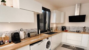 A modern kitchen with white cabinetry, a built-in dishwasher, a coffee maker, and a TV mounted above the sink. - House near Paris • Private Jacuzzi • 7 passengers (Sarcelles)