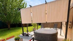 An outdoor patio with a table and chairs, a cushioned seating area, and a pergola providing shade. - House near Paris • Private Jacuzzi • 7 passengers (Sarcelles)