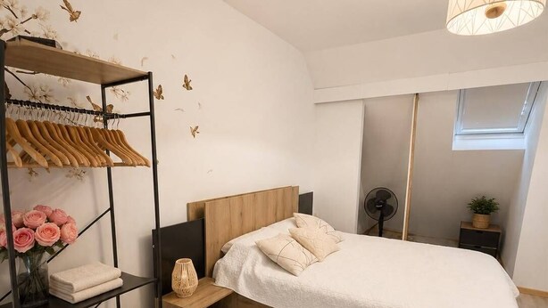 A modern bedroom with a bed, a wooden nightstand, a round rug, a wall-mounted shelf with clothes and flowers, and a ceiling fan. - House near Paris • Private Jacuzzi • 7 passengers (Sarcelles)